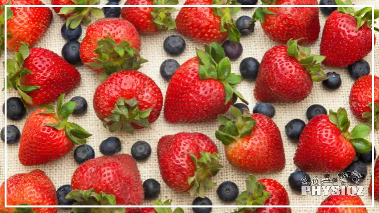 An arrangement of fresh blueberries and strawberries are laying on a white table cloth. 