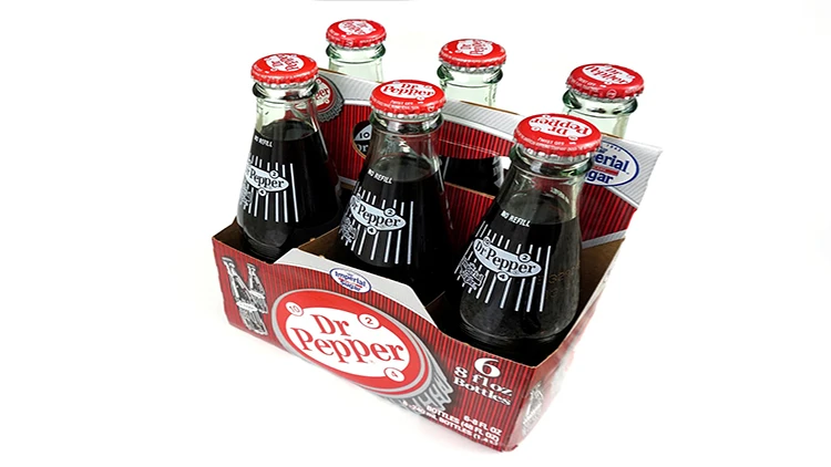 Six unopened and full bottles of Dr Pepper in a to-go packaging on a white background.