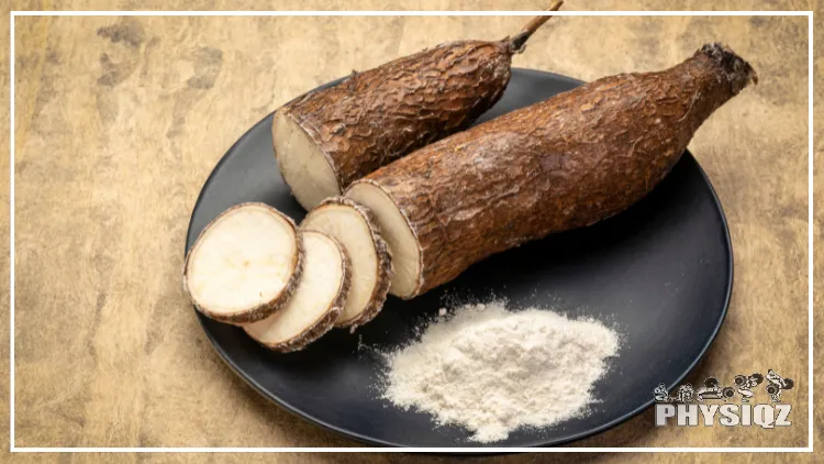 Two cassava plants are sitting on a black plate and have been sliced a few times and next to cassava flour. 