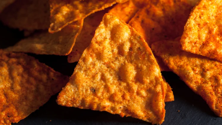 A closeup of triangle-shaped chips or tortilla chips with chili coating giving it a bright orange appearance, placed on top of a black surface.