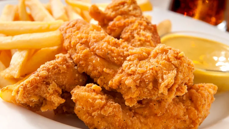Crispy chicken fingers served with a side of golden fries and a small bowl of creamy cheese sauce for dipping.