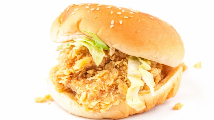 A crispy chicken sandwich with lettuce and sesame seeds sprinkled on top of the buns, the chicken patty is golden brown and appears crispy, with lettuce leaves peeking out from the sides of the sandwich.