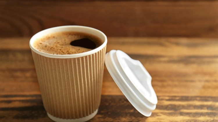 An opened brown and white to-go paper cup filled with dark coffee, displayed on top of a wooden surface.