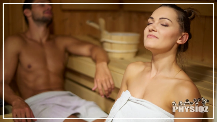 A man with a towel around his waist is blurred in the background and has his left arm resting on a shelf while a woman in the foreground has a white towel around her entire body while sitting on a woodened paneled sauna and wondering "Does sitting in the sauna burn calories or is there really any health benefits?". arm resting on a shelf and a women, both wearing white towels, are sitting in a wood paneled sauna with their heads leaned back and eyes closed.