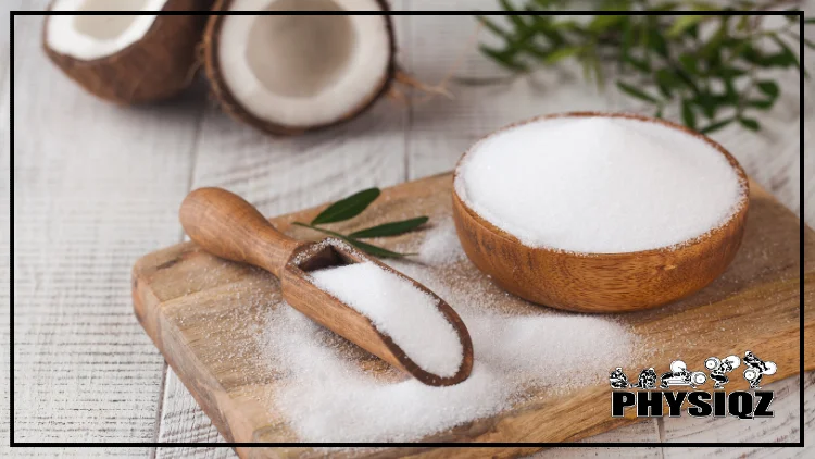 On top of a wooden board is wooden scooping utensil and a wooden bowl filled with erythritol, and there are coconuts in the background.