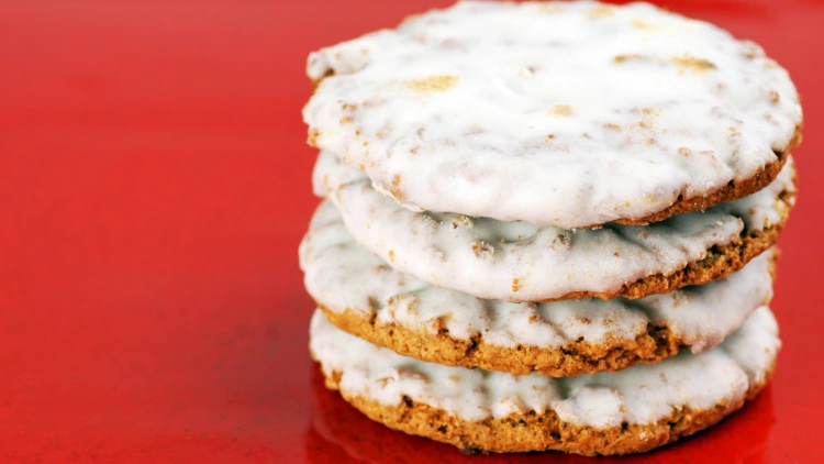 Four cookies with white frosting piled up like a tower on a shiny red surface.