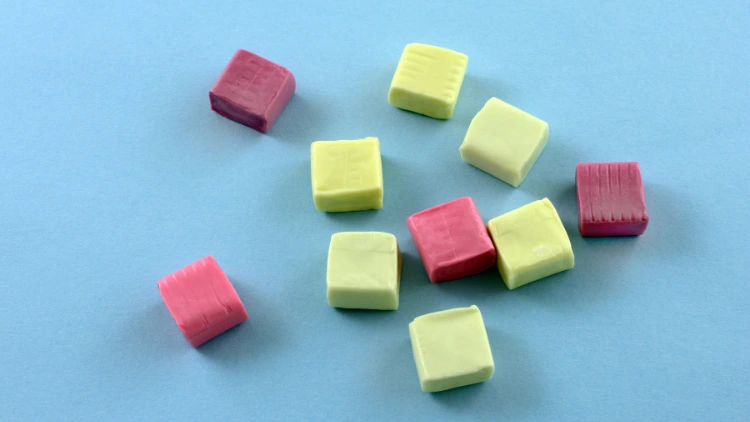 On a blue matte surface, ten pieces of fruit chews candies, four pieces are in color magenta while the other six are in color light green, indicating two different flavors.