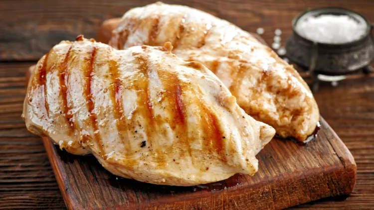 Two pieces of grilled chicken fillet served on a wooden board and displayed on top of a wooden surface.