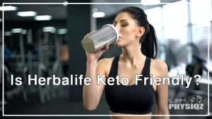 A woman wearing a black tank top is drinking a protein shake from a clear black bottle while wondering about Herbalife shakes carbs content, in a gym.