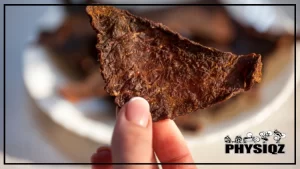 A person is holding a piece of beef jerky from a plate filled with other pieces of beef jerky, which are blurred in the background, as they wonder, "is beef jerky keto-friendly?".
