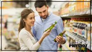 A woman wearing a white long sleeved shirt is standing beside a man in a light blue button up and are both reading the back side of olive oil bottles wondering "Is olive oil keto approved" while standing in a grocery store aisle.