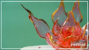 A red translucent flower candy sculpture made out of isomalt keto friendly crystals and is on top of a yellow to white cake that has red speckles of isolmalt on it too.