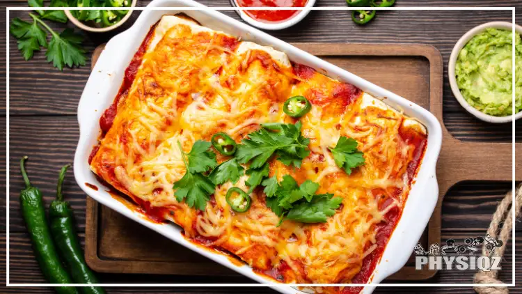 A keto Mexican casserole made with chicken strips, cheese and garnished with basil and pepper served on a white pan and displayed on top of a wooden board, there's a bowl of guacamole and tomato sauce in the background, as well as chilis.