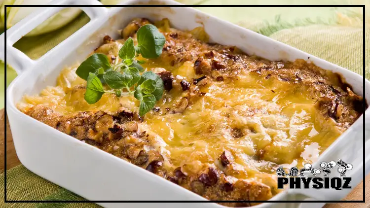 A baked meaty and cheesy casserole is inside of a white ceramic serving dish sitting on top of a green table cloth. 