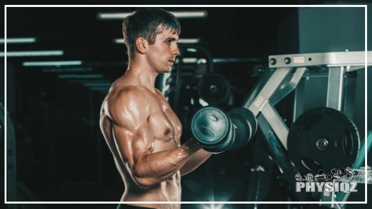 A white, shirtless male with a short haircut is sweating as he curls 10 pound dumbbells inside a commercial gym that has an iso-lateral chest bench press machine in the background. 