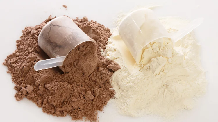 Two scoops of protein powders in different flavors, milk and chocolate, both powders are spilled over the white surface.