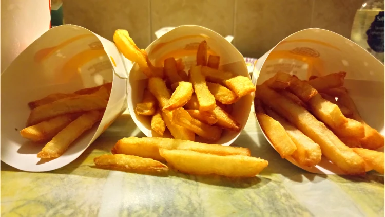 Three cardboard containers filled with hot, crispy French fries from Burger King, each container has the Burger King logo printed on the front and is open at the top to reveal a generous serving of fries inside, the fries are golden-brown and appear to be freshly cooked, with steam rising from them.