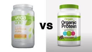 A side-by-side comparison of Vega vs Orgain protein powders, on the left is a white and green colored container of Vega protein powder in vanilla chai flavor, and on the right, is also a green and white colored container of Orgain organic protein powder in chocolate flavor.
