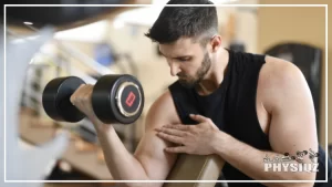 A man with a buzz cut and chin-strap like facial hair is performing a dumbbell preacher curl with his right arm and his left is touching his bicep as he's wondering "Why won't my arms grow"?.