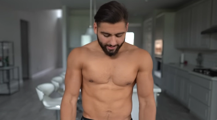 Aseel's is in his kitchen that has all white cabinets, floors, and counter tops while shirtless and his chest looks fairly tones, but small. 