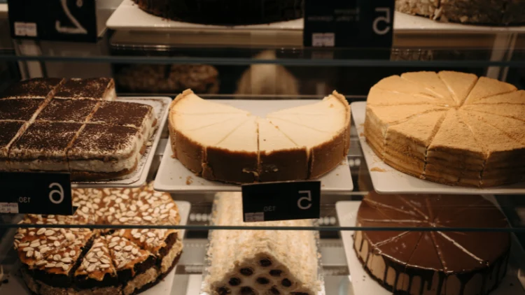 Three shelves in a store that are full of baked goods and desserts such as assorted cakes.