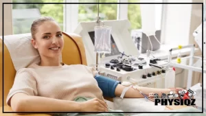 A woman in a tan sweater is smiling while she has a blue blood pressure cuff around her left arm and a tube of blood being pumped to a machine which makes her wonder "Does donating plasma affect muscle growth and gym performance?".