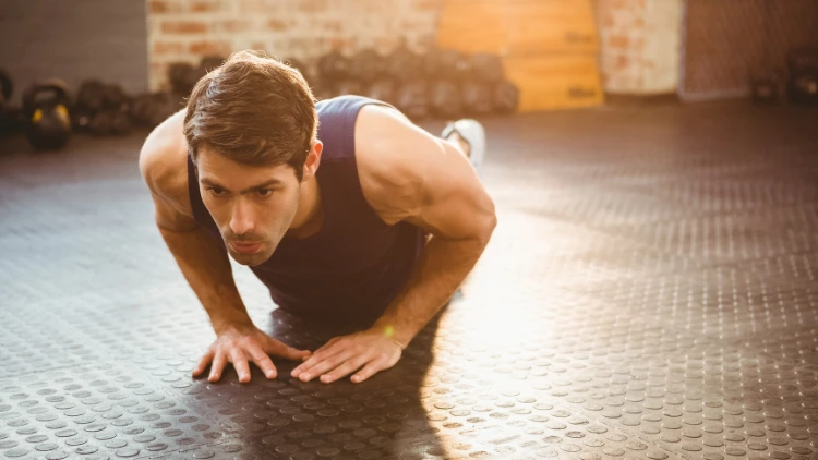 A man with a blue tank top is performing diamond push-ups on a circle pattern floor.