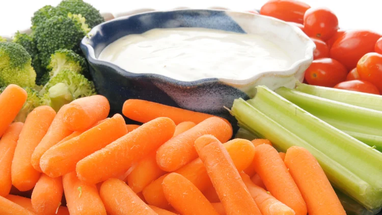 An appetizing vegetable tray is displayed, featuring a variety of fresh and colorful vegetables arranged around a bowl of ranch dressing in the center, the vegetables include baby carrots, broccoli florets, celery sticks, and cherry tomatoes, all meticulously cleaned and cut to bite-sized portions, the colors of the vegetables are vibrant and eye-catching, with shades of green, orange, and red that complement each other beautifully, the creamy white ranch dressing sits in the center of the tray, inviting the viewer to dip the vegetables into it. 