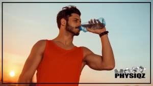 A bearded, fit young man with a black watch on his left arm is wearing a red tank top and drinking water from a clear plastic bottle; he is wondering, 'Is Propel Water good for losing weight?' after jogging outdoors with a view of the sunset in the background.