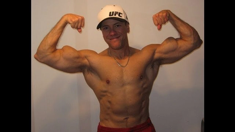 A white muscular guy wearing a white hat with the words UFC on it is flexing in a front double bi that shows his uneven bicep peaks. 