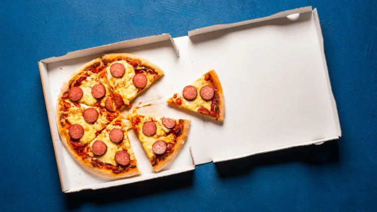 Open box of sliced pizza with pepperoni and cheese in a blue background.