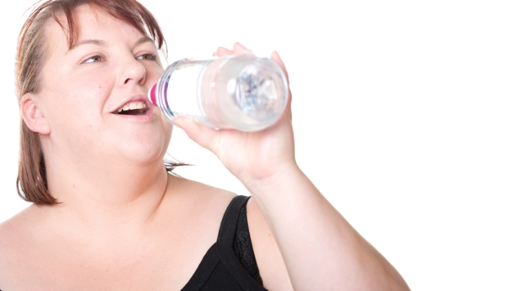 An overweight woman wearing a black tank top is about to drink a water from a clear plastic bottle.