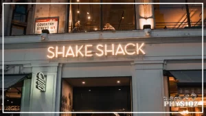A store with classical white concrete columns with a signage saying, 'Coventry Street' and a store sign in led lights that says, 'Shake Shack' and below it on the left corner is a lit-up store logo, makes passersby wonder if there is a Shake Shack gluten free menu available.