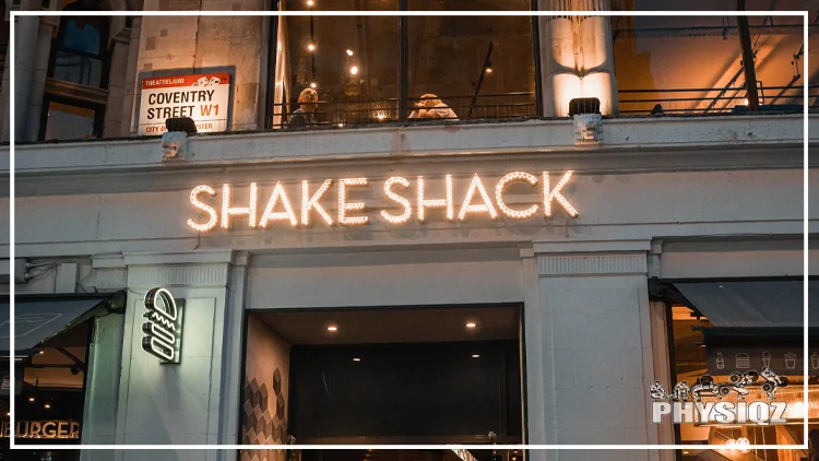 A store with classical white concrete columns with a signage saying, 'Coventry Street' and a store sign in led lights that says, 'Shake Shack' and below it on the left corner is a lit-up store logo, makes passersby wonder if there is a Shake Shack gluten free menu available.