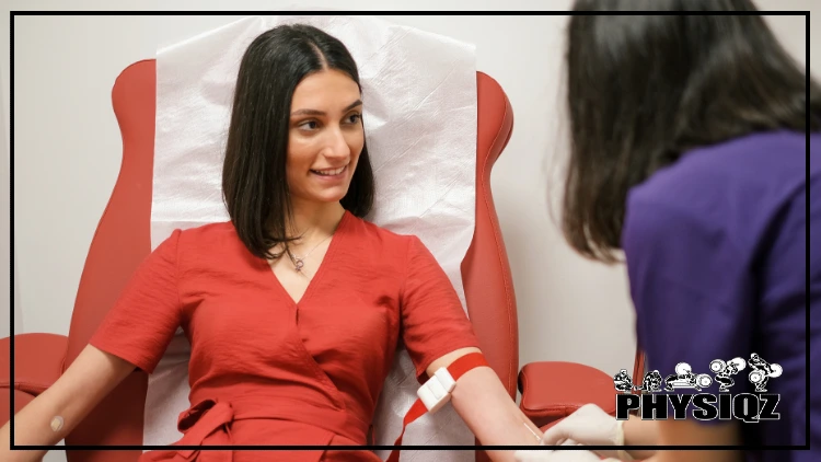 A woman wearing purple top is inserting a needle into another woman's arm who's wearing a red dress and has a tourniquet around her arm.