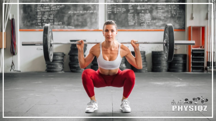 Inside a gym that has a chalk board in the background, a woman is preforming a back squat with a barbell loaded with one 45 lb plate on each side for a total of 135 and she's wearing a white tank top, white shoes, and red leggings. 