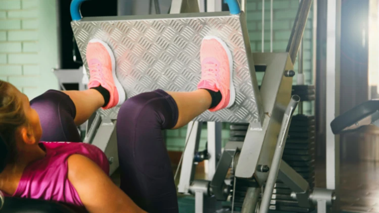 A woman wearing pink top, black pants and pink shoes with black socks performing a leg press.