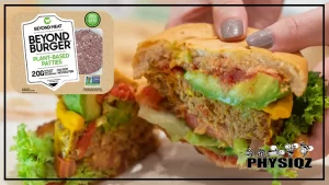 A person with their nails painted grey is holding up a plant based burger patty that's in between an avocado, lettuce, cheese, and a bun while wondering "Are Beyond Burgers keto?, and the burger is cut in half with the second half resting in the background and a Beyond Burger logo at the top right.