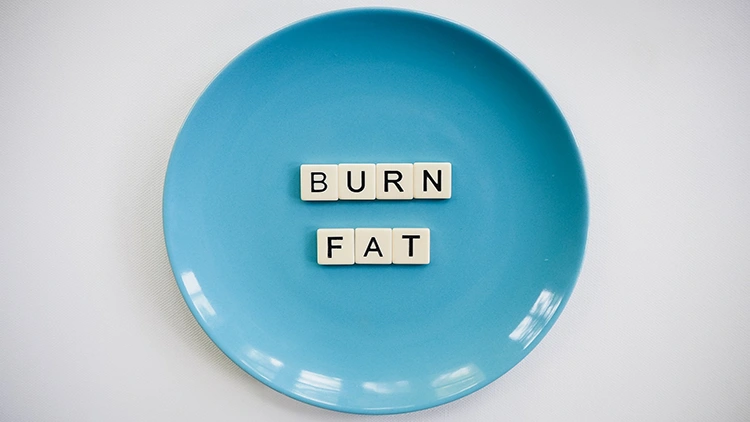 Letter tiles that form the word burn fat placed on a blue ceramic plate on a white surface.