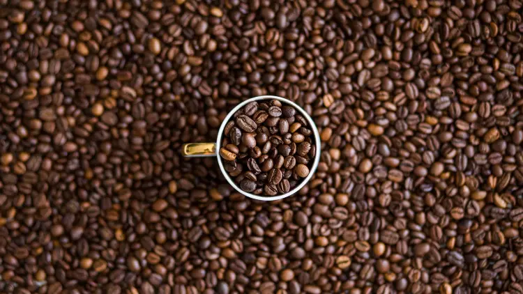 A silver cup of coffee beans on top of a large pile of more coffee beans.