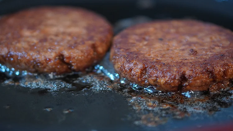 Two burger patties cooked with a sizzling oil.