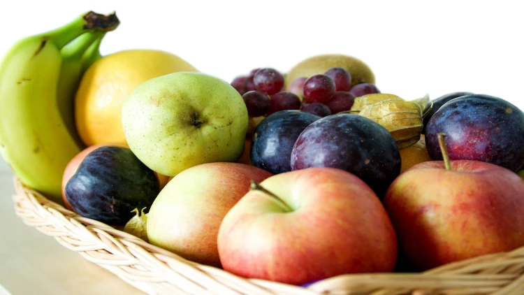 A basket filled with variety of fruits such as apples, banana, plums, oranges, kiwi and grapes.