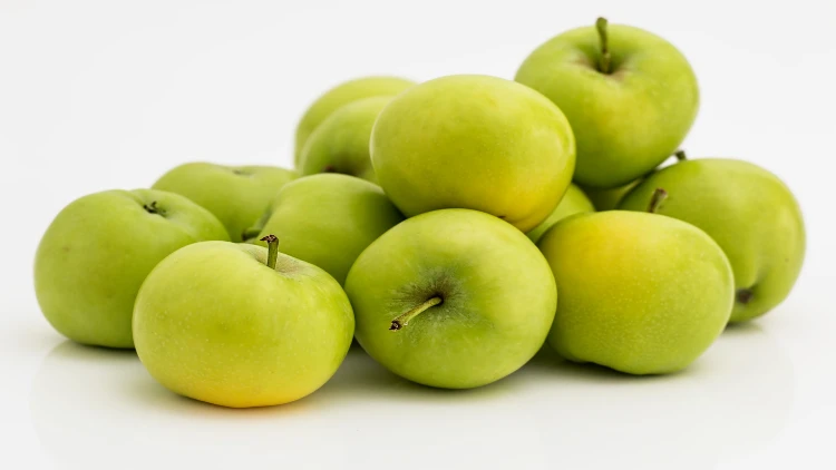 Thirteen green apples stacked on top of each other and sitting on top of a shiny white surface.