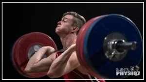 A muscular man is shown lifting weights with a look of intense concentration on his face, he wears a black tank top and is holding blue and red weights up to his shoulders, appearing to struggle with the weight, the background is black, emphasizing the focus on the man and his weightlifting.