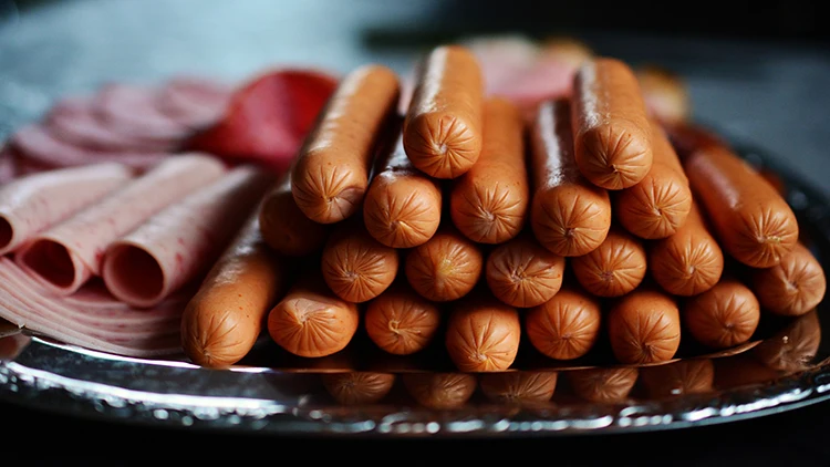 Twenty-one hotdogs and slices of ham served in a silver platter on top of a dark-colored surface.
