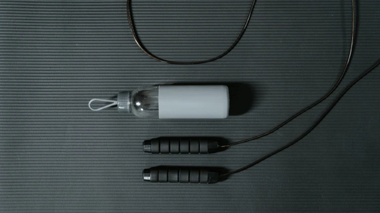 A black jump rope and grey water bottle on a black yoga mat.