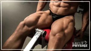 A shirtless bodybuilder in black shorts is on a red machine doing one of his favorite outer quad exercises, a leg extension, and this shows his tan and large outer thighs as well as quad sweep since he's lean.