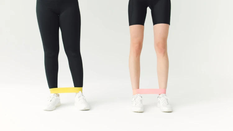 Two people wearing black bottoms and white shoes working out using yellow and pink resistance bands.