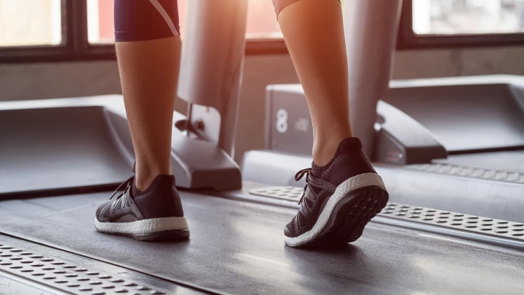 A person wearing black pants and shoes using a treadmill beside another treadmill.