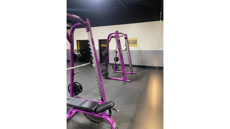 Two purple Smith machines in a gym called Planet Fitness, with grey floor and white walls.